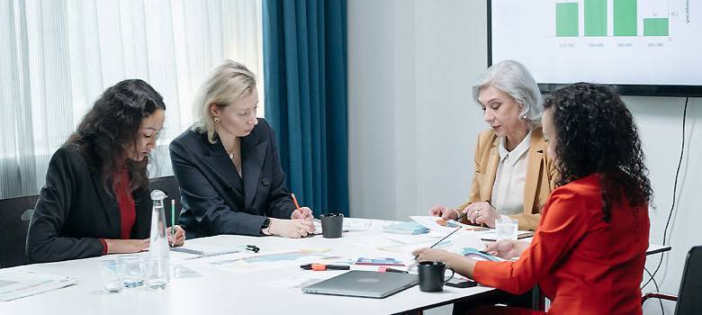four business women sit around a table going over documents